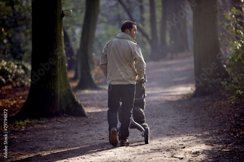 Photo: A young father pushing a stroller in the park, rear view A young father pushing a stroller in the park, rear view