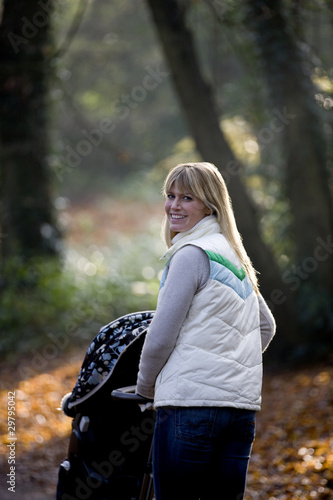 Photo: A young mother pushing a stroller in the park, smiling A young mother pushing a stroller in the park, smiling