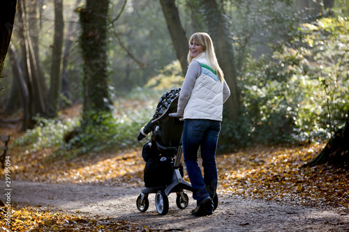 Photo: A young mother pushing a stroller in the park, smiling A young mother pushing a stroller in the park, smiling