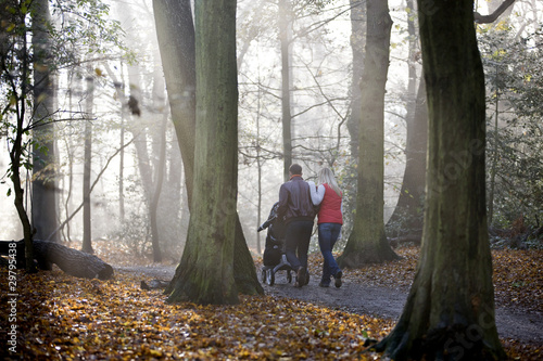 Photo: A young couple pushing a stroller in the park, rear view A young couple pushing a stroller in the park, rear view