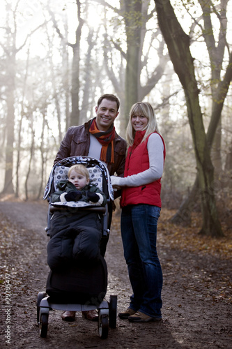 Photo: A young couple pushing a stroller in the park, smiling A young couple pushing a stroller in the park, smiling