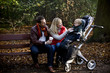 A young couple on a bench, smiling at their son in a stroller