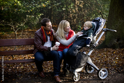 Photo: A young couple on a bench, smiling at their son in a stroller A young couple on a bench, smiling at their son in a stroller