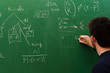 Young student writing formulas on green chalk board