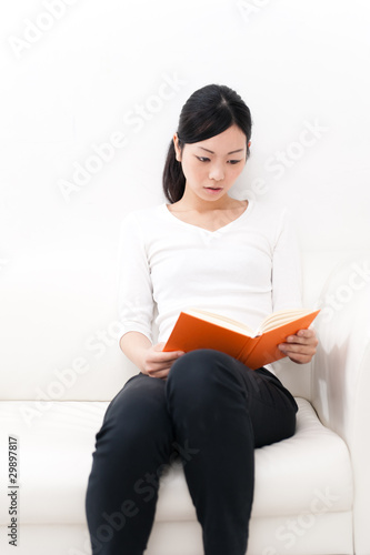 Photo: beautiful asian woman reading a book on the couch beautiful asian woman reading a book on the couch