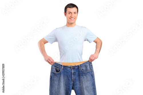 Photo: Portrait of a weight loss male showing his old jeans Portrait of a weight loss male showing his old jeans