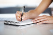 Female hand writing notes on notepad at desk