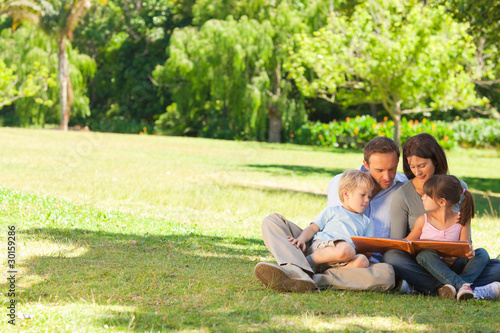 Photo: Family looking at their photo album in the park Family looking at their photo album in the park