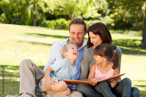 Photo: Family looking at their photo album in the park Family looking at their photo album in the park