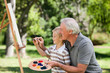 Happy Grandfather and his grandson painting in the garden Happy Grandfather and his grandson painting in the garden
