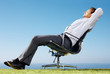 Businessman sitting relaxed on chair against sky