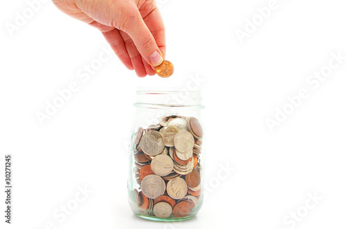 Photo: hand putting penny in a coin jar, saving money hand putting penny in a coin jar, saving money