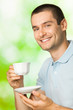 Portrait of young happy smiling man drinking coffee, outdoors
