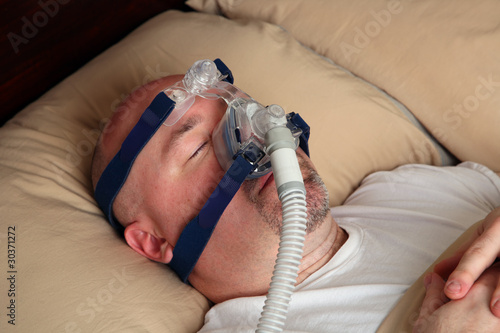Foto: Man with sleep apnea using a CPAP machine in bed. Man with sleep apnea using a CPAP machine in bed.