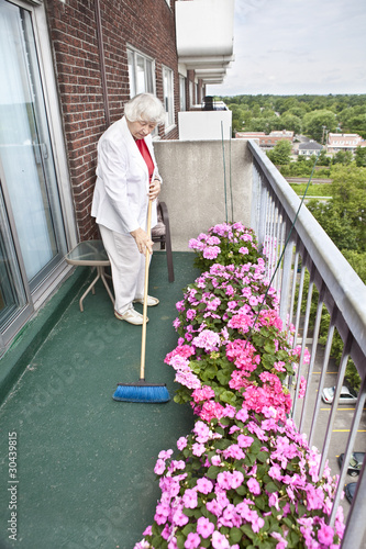 Photo: Senior woman brooming her balcony Senior woman brooming her balcony
