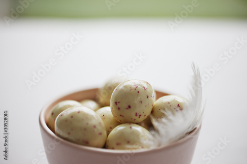 Foto: Speckled candy eggs in bowl with feather Speckled candy eggs in bowl with feather