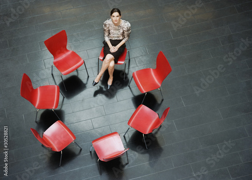 Photo: Businesswoman sitting alone in circle of chairs Businesswoman sitting alone in circle of chairs