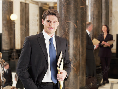 Foto: Smiling businessman leaning against pillar in corridor Smiling businessman leaning against pillar in corridor