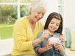 Grandmother putting coin into granddaughter?s piggy bank