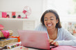 Smiling teenage girl using laptop in bedroom