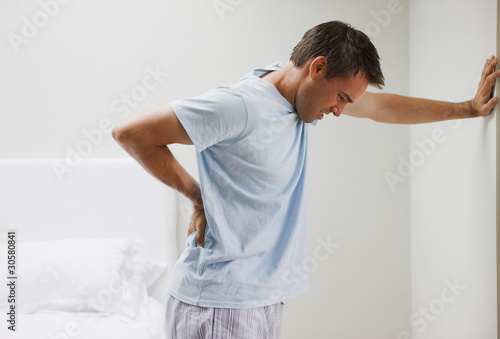 Photo: Man with backache leaning against wall Man with backache leaning against wall