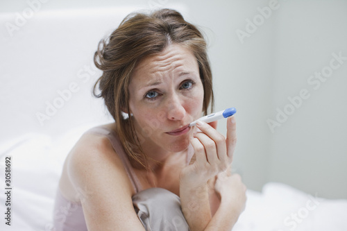 Photo: Sick woman taking temperature with digital thermometer Sick woman taking temperature with digital thermometer