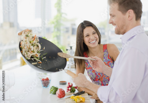 Foto: Woman watching husband flipping stirfry in the kitchen Woman watching husband flipping stirfry in the kitchen