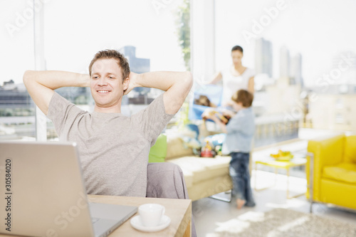 Foto: Man using laptop with family in background Man using laptop with family in background