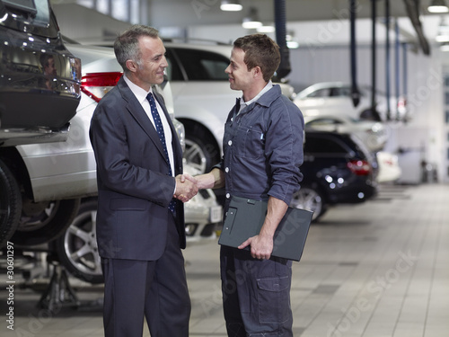 Photo: Businessman shaking hands with mechanic in auto repair shop Businessman shaking hands with mechanic in auto repair shop