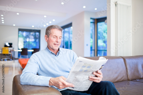 Photo: Man reading newspaper on couch Man reading newspaper on couch