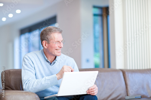 Photo: Smiling man using laptop on couch Smiling man using laptop on couch