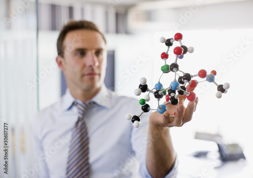 Photo: Businessman holding molecule model in office Businessman holding molecule model in office