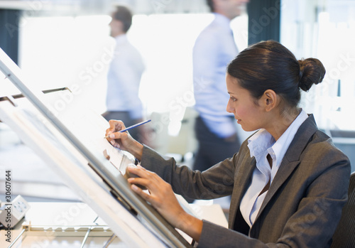 Photo: Businesswoman drawing on drafting table in office Businesswoman drawing on drafting table in office