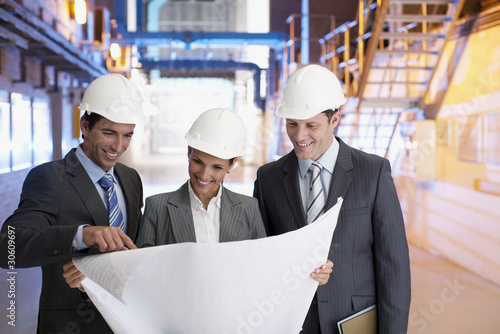 Photo: Business people reviewing blueprints in factory Business people reviewing blueprints in factory