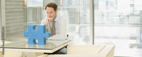Photo: Businessman looking at jigsaw puzzle piece Businessman looking at jigsaw puzzle piece