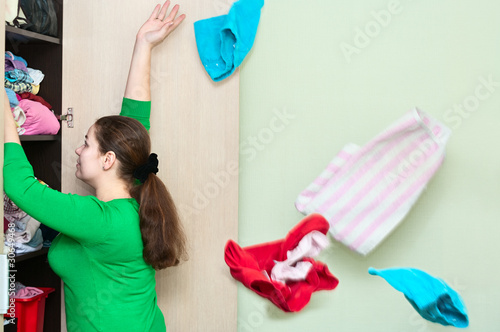 Photo: Young caucasian woman throwing clothes from wardrobe back Young caucasian woman throwing clothes from wardrobe back