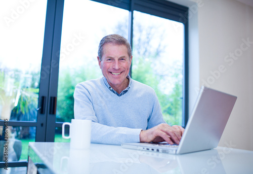 Foto: Smiling man using laptop at table Smiling man using laptop at table