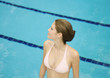 Woman standing in pool by pool, looking to the side, high angle view