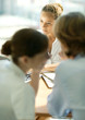 Photo: Young couple sitting across table from young female professional, woman whispering to man Young couple sitting across table from young female professional, woman whispering to man