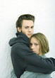Young couple embracing, looking at camera, white background