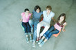 Four teen friends sitting on cushions on ground, looking at camera, high angle view