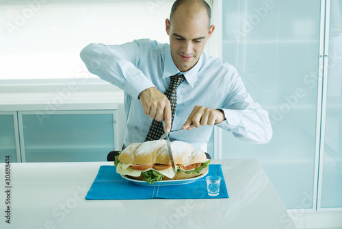 Photo: Man cutting into large sandwich with knife and fork Man cutting into large sandwich with knife and fork