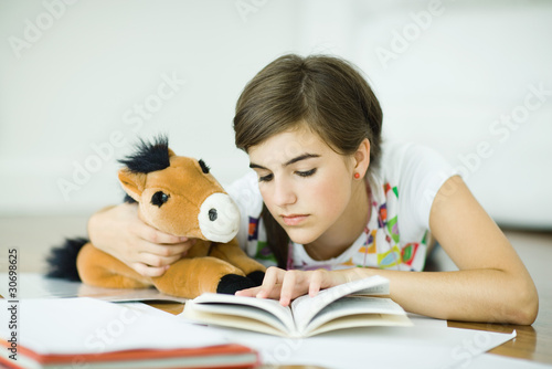 Photo: Teen girl lying on floor, holding stuffed toy horse and doing homework Teen girl lying on floor, holding stuffed toy horse and doing homework