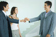 Real estate agent holding out keys to young couple, standing in bare home interior