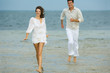 Photo: Man and young female companion on beach, hurrying toward camera, smiling, man in background, full length Man and young female companion on beach, hurrying toward camera, smiling, man in background, full length