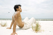 Foto: Barechested man sitting on beach, holding blade of grass in mouth, full length Barechested man sitting on beach, holding blade of grass in mouth, full length