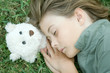 Boy lying in grass with eyes closed, head resting on teddy bear