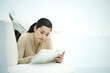 Young woman lying on couch, reading book