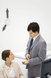 Photo: Male supervisor standing beside female employee, pointing at wristwatch, clock hands on wall in background Male supervisor standing beside female employee, pointing at wristwatch, clock hands on wall in background