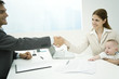 Professional woman with baby shaking hands with businessman, sitting at desk